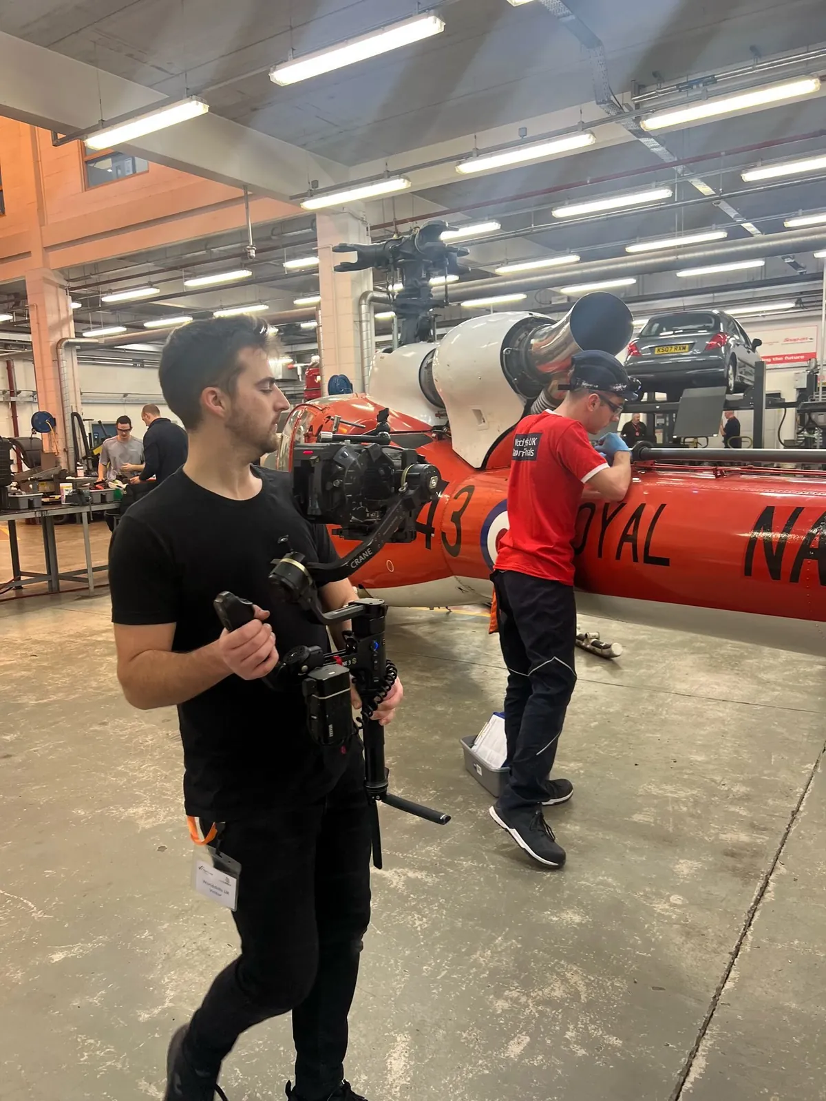 A camera operator walks a gimbal rig into position during a filming day in an aircraft hangar