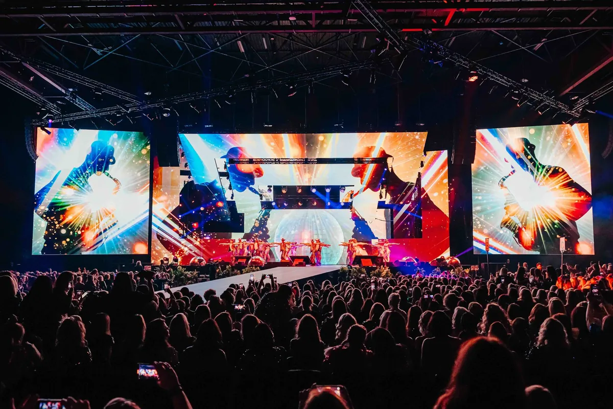 The Glammies arena audience bathed in red light beneath large LED screens showing bold silhouette graphics